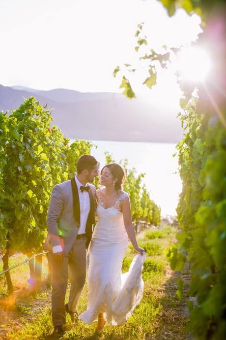 Newlyweds strolling together between vineyard rows with the sun setting over the lake in Kelowna