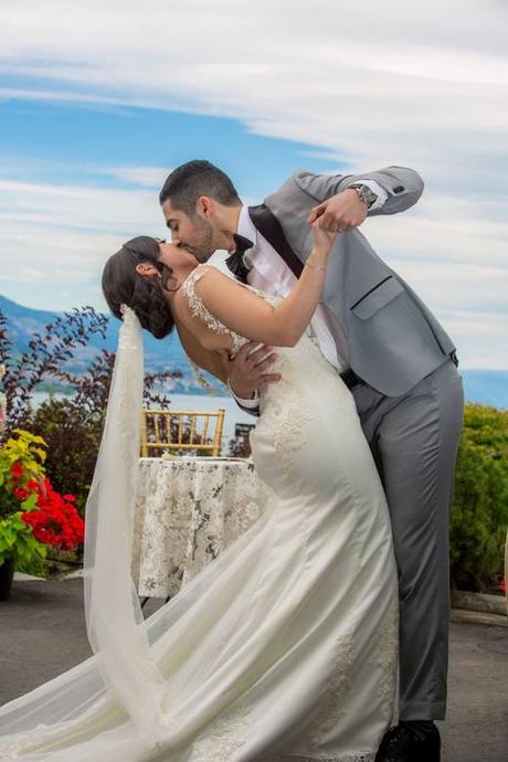 Newlyweds sharing a playful dip and kiss with hills and a lake in the background