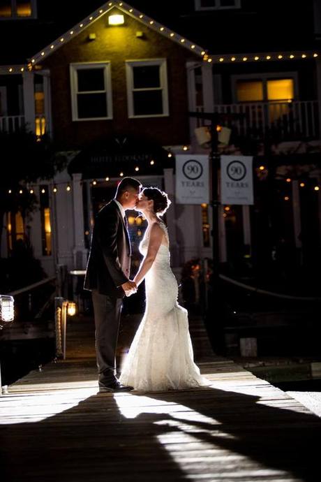 Bride and groom sharing a quiet kiss under string lights on a dock at night