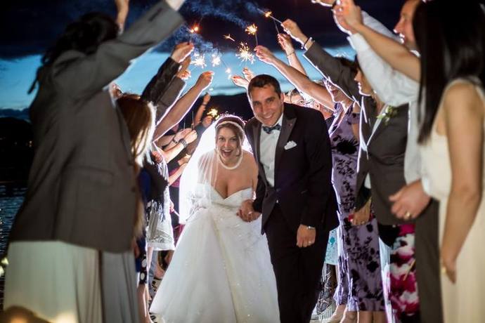 Bride and groom smiling as they walk beneath an arch of sparklers held by wedding guests