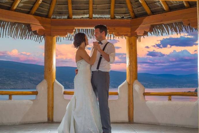 Bride and groom dancing under a timber gazebo at sunset overlooking the water near Kelowna, BC
