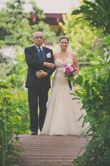 Bride walking arm in arm with an older gentleman along a garden pathway before an outdoor wedding ceremony