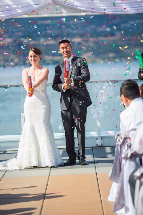 Newlyweds celebrating with colourful confetti cannons at an outdoor wedding overlooking the water