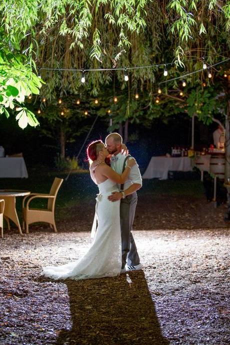 Newlyweds kissing beneath hanging string lights during an outdoor evening wedding reception