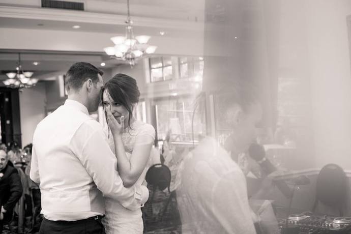 Black-and-white candid moment of a bride wiping away a tear as her partner leans close during a wedding reception