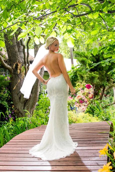 Bride holding a pink bouquet and looking over her shoulder among green trees