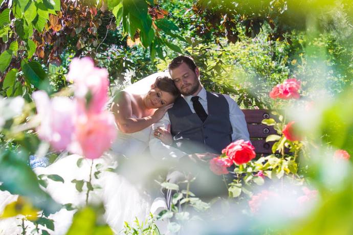 Wedding couple resting together on a garden bench framed by soft pink roses
