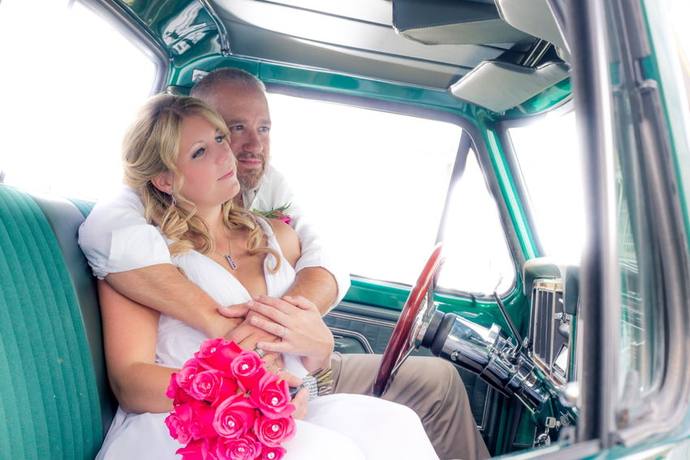 Wedding couple embracing inside a vintage turquoise truck with a bouquet of pink roses