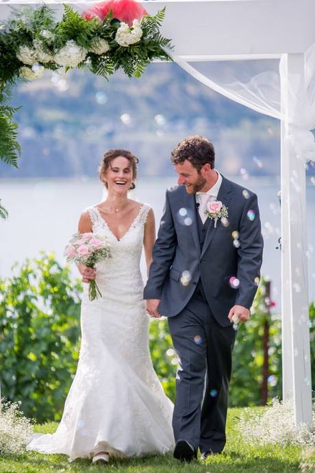 Newlyweds smiling together as bubbles float through an outdoor Penticton wedding ceremony