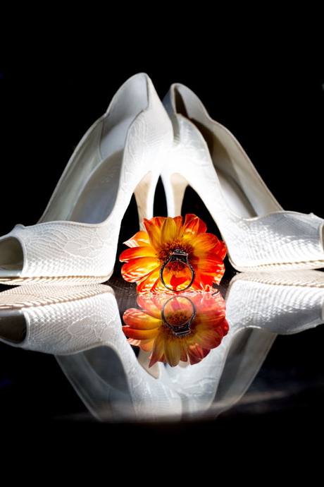Wedding ring resting on an orange flower between white bridal shoes in Penticton